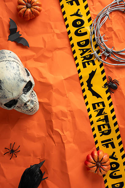 istock Festive vertical Halloween decor featuring a skull, pumpkins, spiders, barbed wire, and warning tape on a vibrant orange background. Perfect for creating a spooky and eerie holiday atmosphere 2224532111