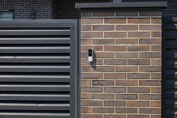 A contemporary intercom is mounted on a brick wall adjacent to a slatted gate in a well-maintained suburban area