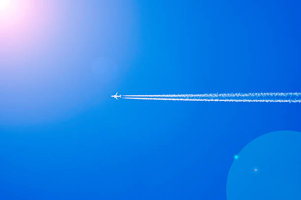 An airplane flying at cruising altitude with a long contrail trailing behind, set against a deep blue sky.