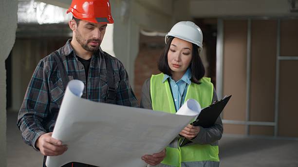 istock Multiethnic builders in uniform discussing blueprint inspection business engineers Caucasian man Korean woman hardhat discuss plan construction building project two workers partners technicians indoor 2224554842