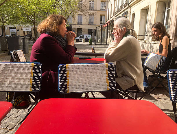 Paris, France - April 9, 2025: Two mature women sit chatting at a sidewalk cafe in the Place Sainte-Catherine in the Marais (4th arrondissement).