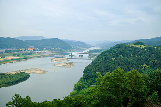 Gongju, South Korea - June 13th 2025: Viewed from Gong Mountain Fortress, the Geum River flows past forested hills and sandbanks, with a pair of bridges connecting Gongju across the water.