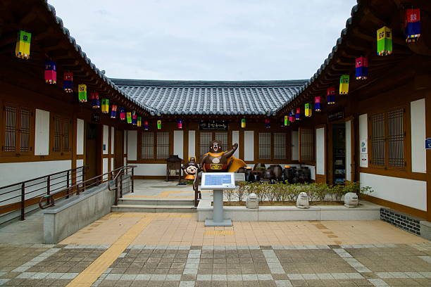 Gongju, South Korea - June 13th 2025: A courtyard in Gongju Hanok Village features traditional architecture, colorful lanterns, and cartoon bear statues in front of onggi jars and a visitor kiosk.