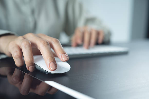 istock Woman hand clicking computer mouse on office table. Business woman working on desktop computer and using wireless mouse, browsing the internet, searching the information, business background, closeup 2224562839