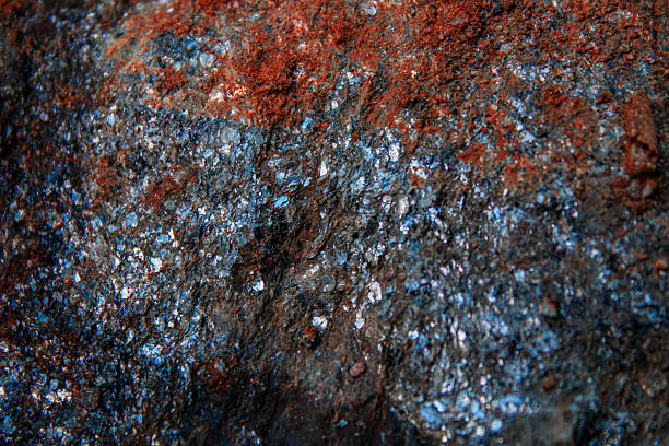 a close-up view of a textured rock surface, with reddish-brown rusty material and shimmering crystal like flakes. abstract background with copy space