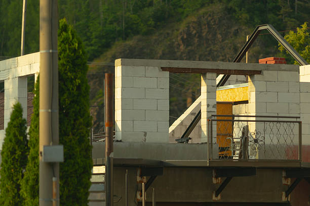 A construction site featuring a building that is currently being constructed. It showcases a balcony, and there are several trees visible in the background