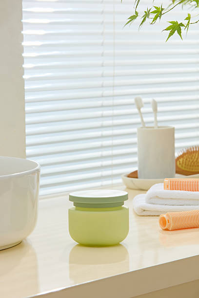 istock Sunlit bathroom corner with soft green containers, white towels, and minimal toothbrush set. Open countertop creates space for placing unbranded cosmetic mockups or 2224583082