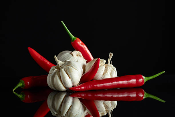 Garlic bulbs and red chili peppers on a black reflective background.
