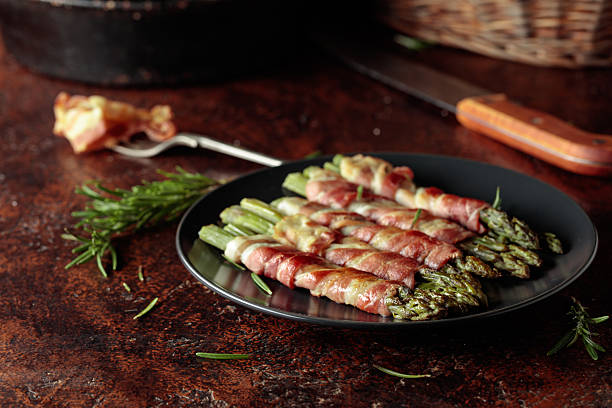 Grilled green asparagus with bacon in black plate on a brown vintage background.