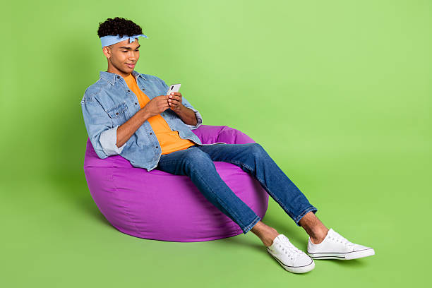 istock Full length body size photo of young guy in beanbag using cellphone app browsing internet isolated on vibrant green color background 2224600956