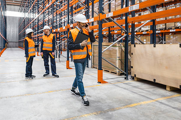 istock Warehouse manager walking and talking on the phone while workers are checking inventory 2224602114