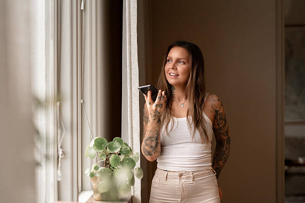 Woman using voice assistant on smartphone by the window at home