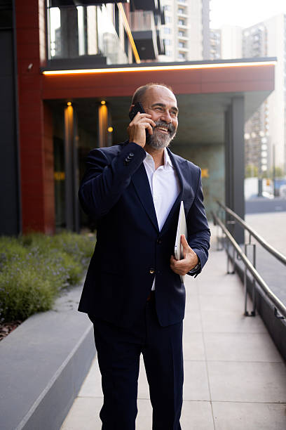 istock Smiling businessman walking and talking on phone outside office 2224604605