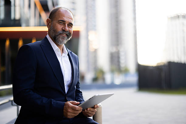 istock Senior businessman using digital tablet while sitting in front of modern office buildings 2224604619