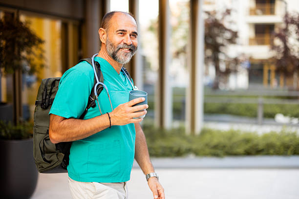 istock Smiling doctor walking with backpack and coffee outside hospital 2224604781