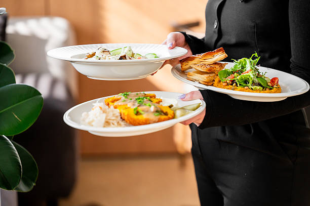 istock Restaurant server in black uniform holding three plates with fresh salad, creamy pasta, and vegetable side dish, against softly lit blurred background. 2224604847