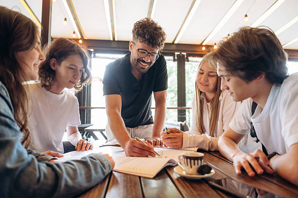 istock Guy in glasses is standing and explaining project plan. Group of young friends are in the cafe restaurant 2224614902
