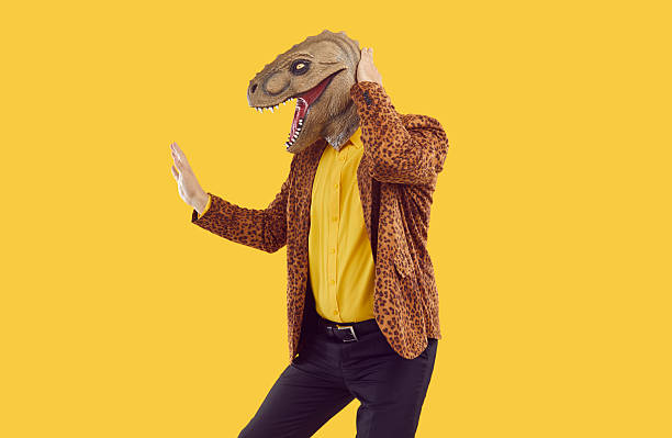 istock Cheerful and eccentric man with dinosaur head dancing isolated on vivid orange background. 2224615956