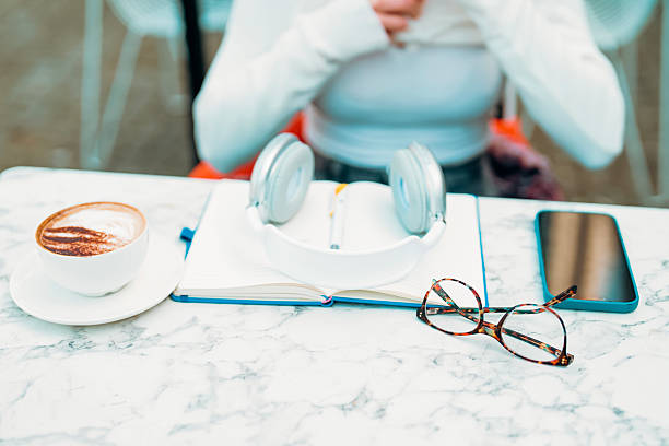 A person sits at a marble table in a cozy cafe, enjoying a cup of warm coffee while preparing to write in a notebook, with headphones nearby.