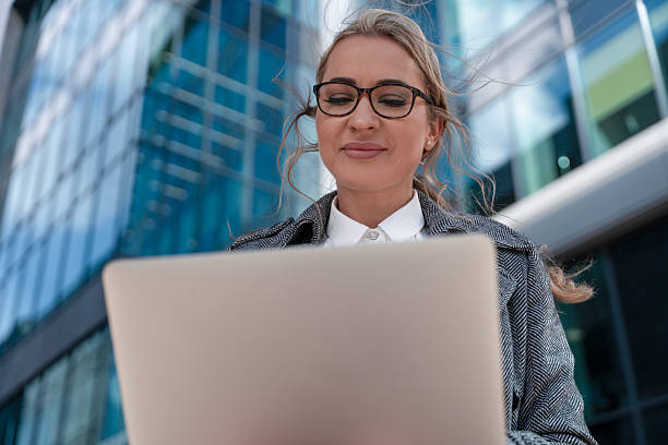 istock Professional woman working on laptop outside modern office building during sunlight hours 2224624681
