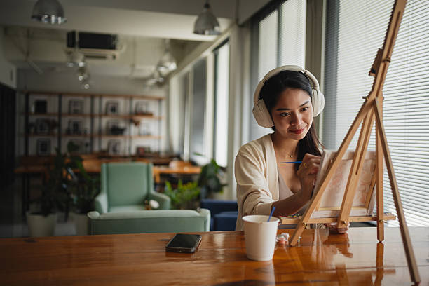 Mid-adult woman is painting on small canvas using an easel at home.