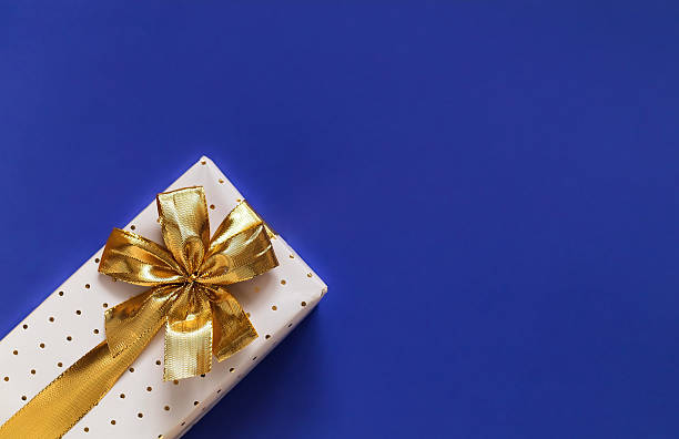 istock White gift box with golden ribbon and bow on a blue background. Top view. Copy space. 2224627082