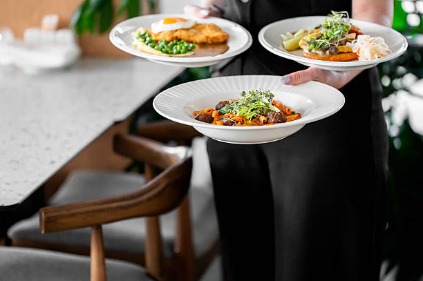 istock Waiter in black uniform holding three restaurant meals including pasta with meatballs, breaded cutlet with egg and mashed potatoes, and vegetables, served in a modern dining setting. 2224633778