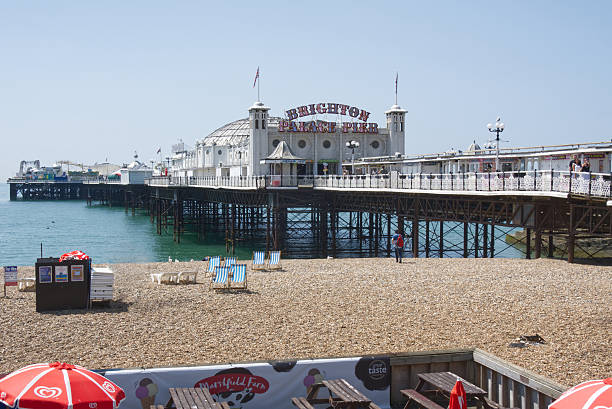 Brighton Palace Pier and shingle beach at Brighton in East Sussex, England. With people and beach side cafe.