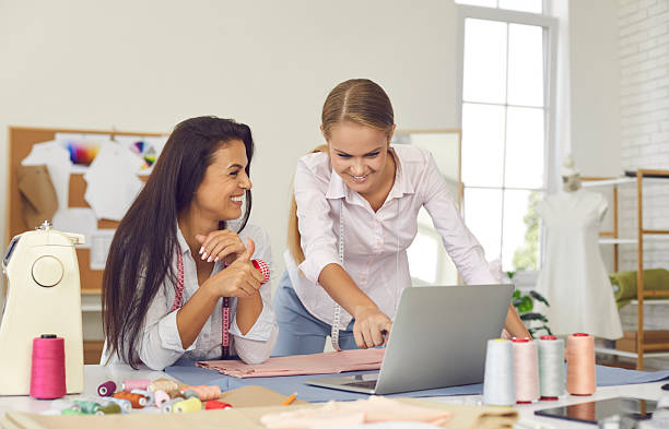 istock Two young female seamstresses in sewing studio check and record customer orders using laptop. 2224636372