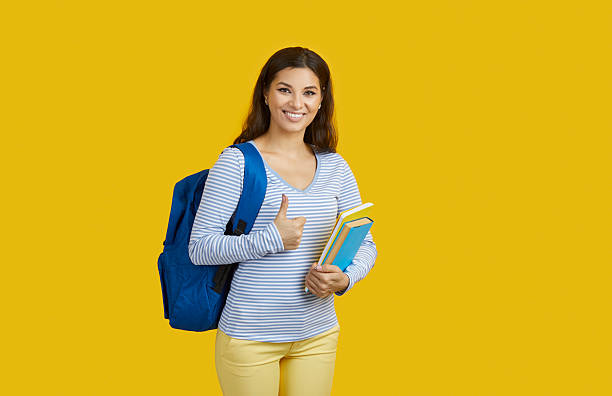 istock Elementary schoolgirl with backpack showing thumb up and smiling on vibrant yellow background, education concept. 2224637514