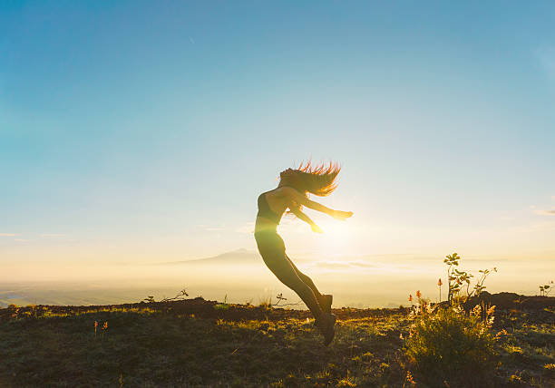 Female hiker jumping in the air celebrating reaching the mountain top at sunrise