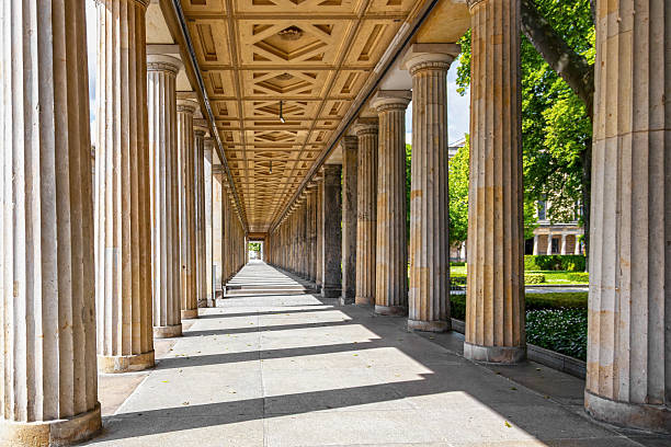istock Historic colonnade with classical stone pillars. Symmetrical view of an ancient-style colonnade with tall fluted columns and ornate ceiling, casting shadows on a sunny day. 2224642930