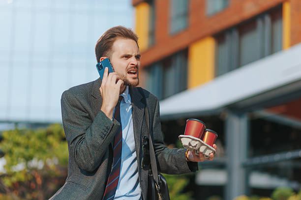 istock Annoyed young man in suit yelling on call with takeaway coffee cups 2224644468