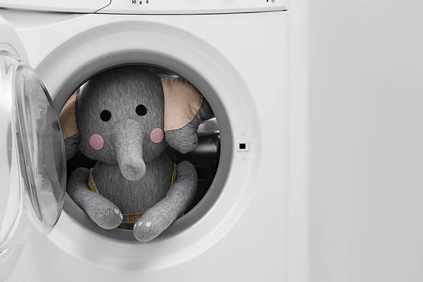 istock Washing machine with toy elephant near light wall, closeup 2224654436