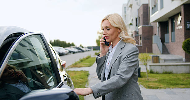 istock Middle-aged woman gets behind the wheel in a car and talking on phone, solving business issues near office. Caucasian girl near white car. 2224662666