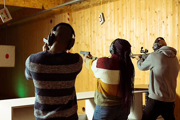 Friends having fun in shooting gallery using guns to hit targets with ammo. Mates entertained by shooting bullseyes at indoor firing range facility, competing against each other