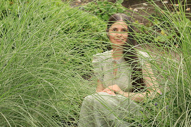 A Ukrainian woman sitting in a patch of tall grass. She is wearing long brown hair, makeup, a pale green short sleeve dress.