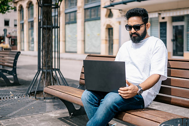 istock Remote worker with laptop sitting on a bench in the city 2224664436