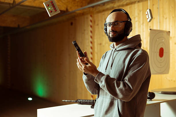Portrait of Middle Eastern man in indoor shooting range offering rental weapons for tryouts, doing training. Arab novice in firing range getting hands on experience with pistol