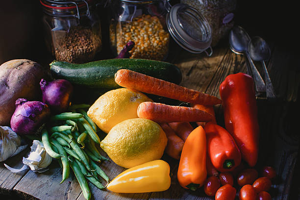A colorful assortment of fresh vegetables including zucchini, carrots, peppers, and garlic is displayed on a wooden table. Glass jars filled with legumes complement the vibrant produce - health benefits, healthy lifestyle