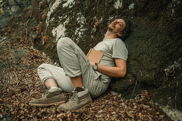 istock Man Resting Outdoors by a Rock with a Notebook in Relaxed Atmosphere 2224667646