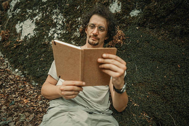 Man Relaxing Outdoors Reading a Book Amidst Natural Surroundings