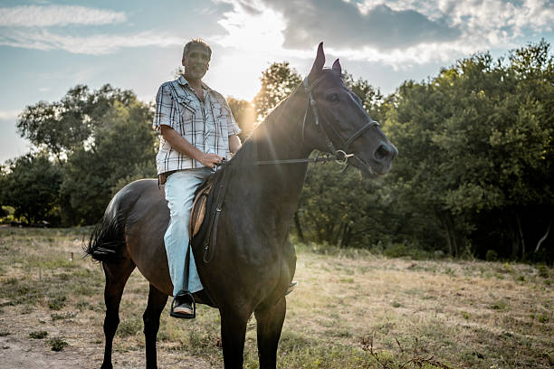 A mature male rides a black horse in a sunny forest clearing, conveying serenity and harmony with nature. The man is casually dressed, while the scene evokes warmth and tranquility.