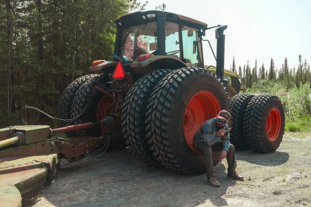 A man sits on a large tractor tire and sends a voice message using a smartphone