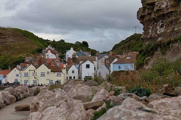 istock A coastal village nestles between rocky cliffs under a cloudy sky. 2224680029
