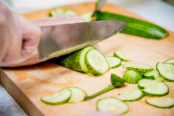 Chef in restaurant in kitchen preparing vegetable salad, close-up hands cutting tomato and cucumber on cutting board