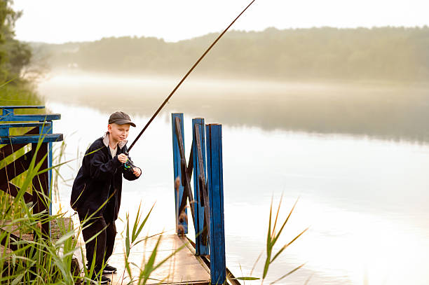Young boy learning to fish alone on a wooden pier by a misty lake