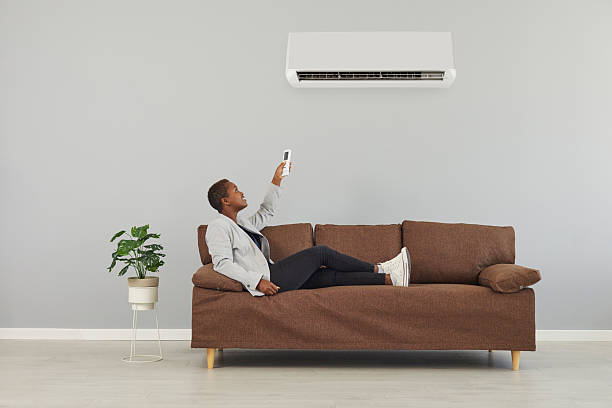 istock Black woman sitting on sofa, holding remote control and switching air conditioner 2224685694
