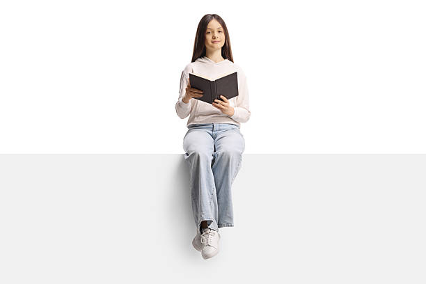 istock Female teenager sitting on a blank panel and holding a book 2224686183