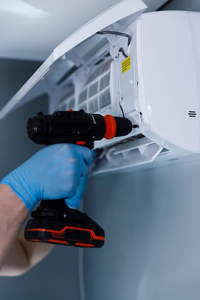istock Hand holding a power drill with a bright orange and black design, set against an air conditioning unit, highlighting the maintenance process being undertaken 2224688730